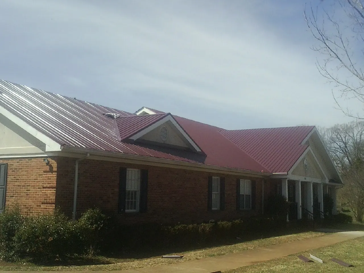 Red metal roof with gabled entries on a long brick building, from a Hail Damage Roof Repair job in Dallas City