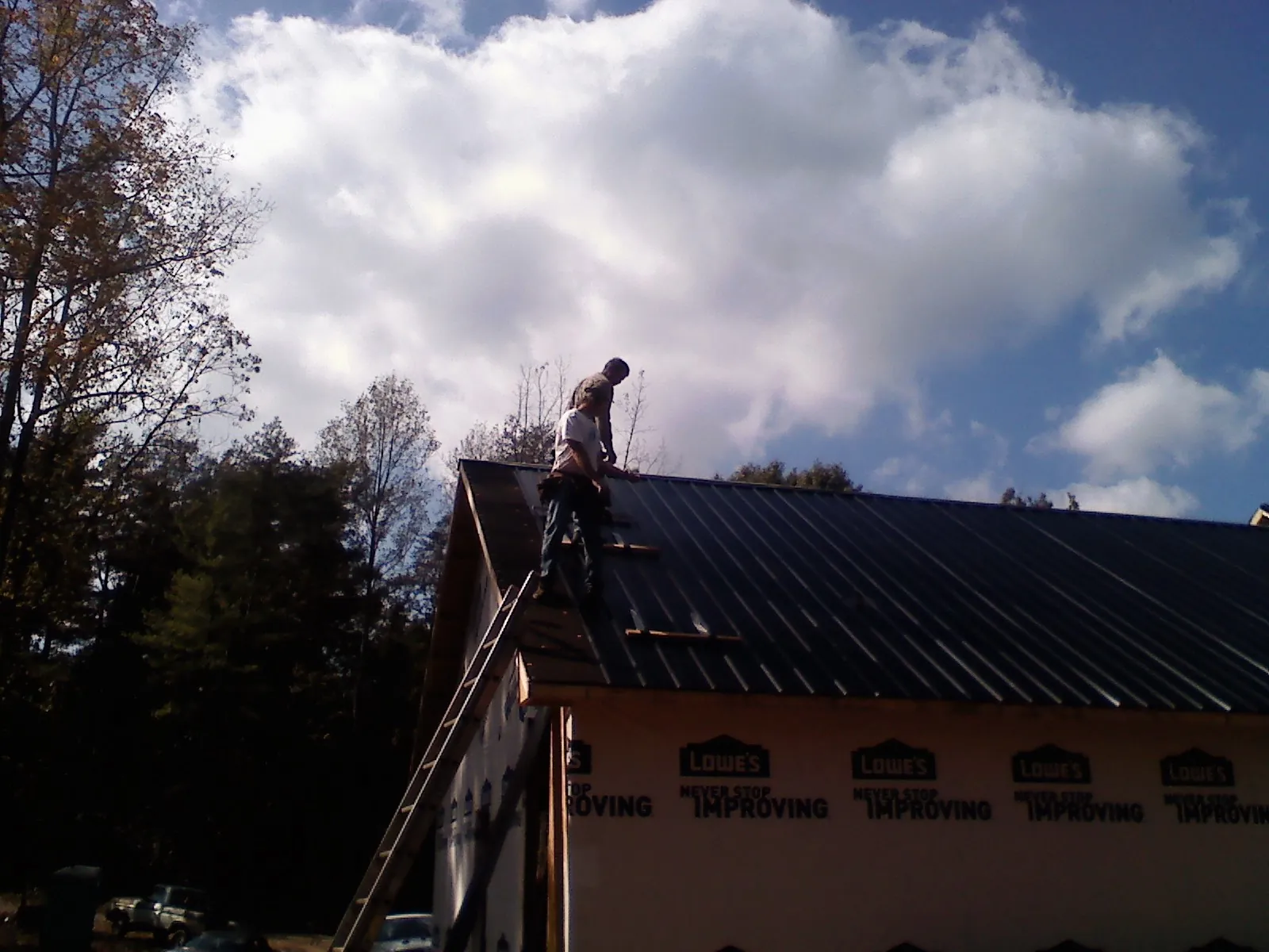 Roofer fastening dark metal panels high against a cloudy sky, from a Roof Inspection job in Dallas City