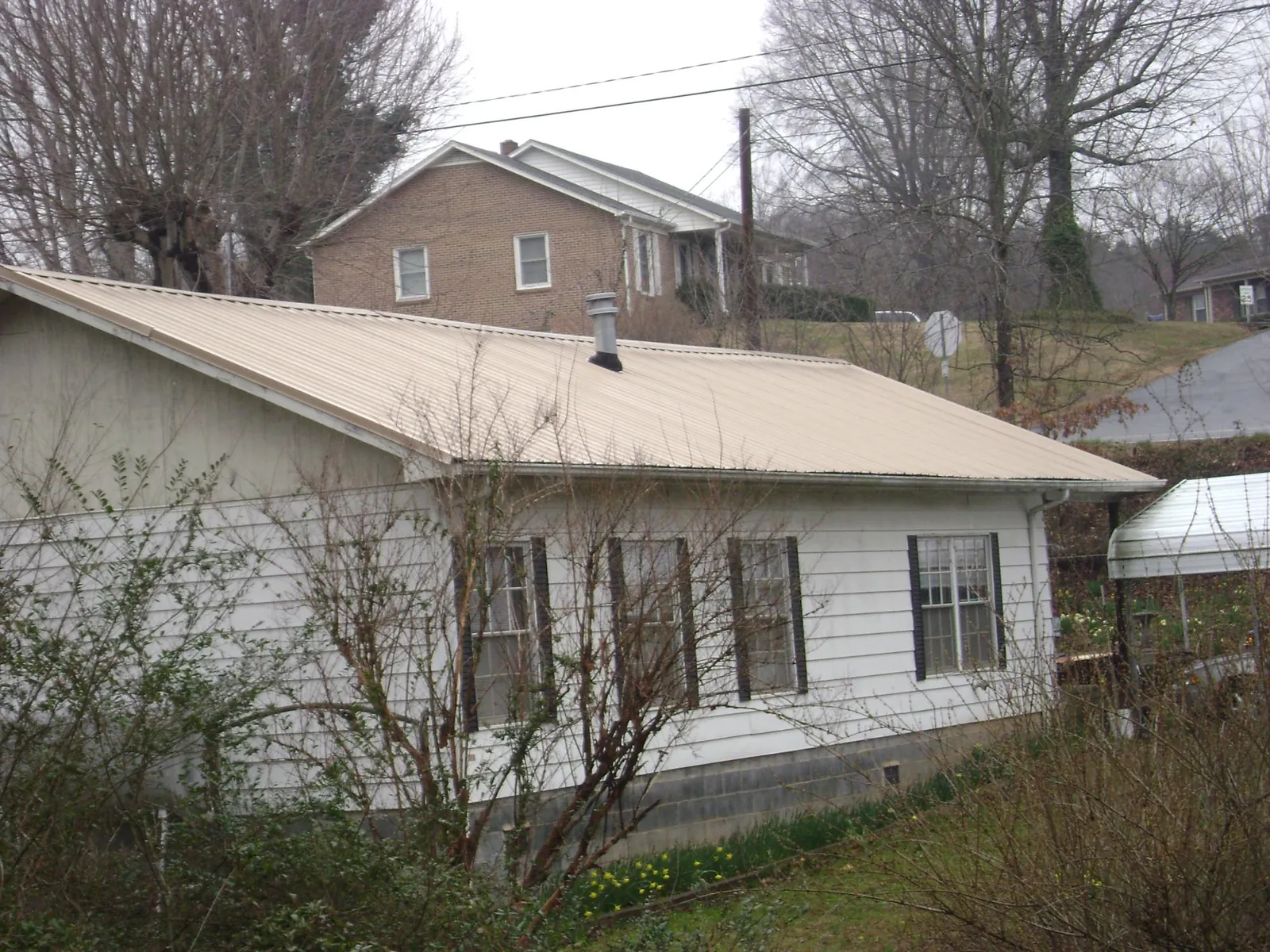 Tan metal roof on a white sided house set into a hillside — Commercial Roofing by Roofing Brothers in Dallas City